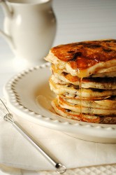 A stack of pancakes on a white plate with syrup running over the top