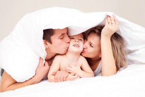Mom, dad, little boy giving kisses in white sheets