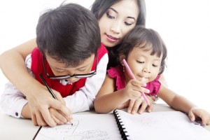 Young Asian mother guiding her children to learn how to write