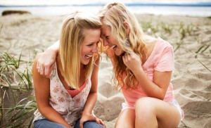Two sisters sitting on the beach laughing