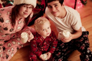 Brothers and sister sitting by Christmas tree with hot chocolate