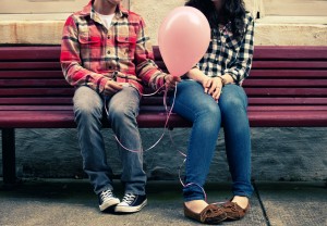 Teen boy giving pink balloon to teen girl on bench